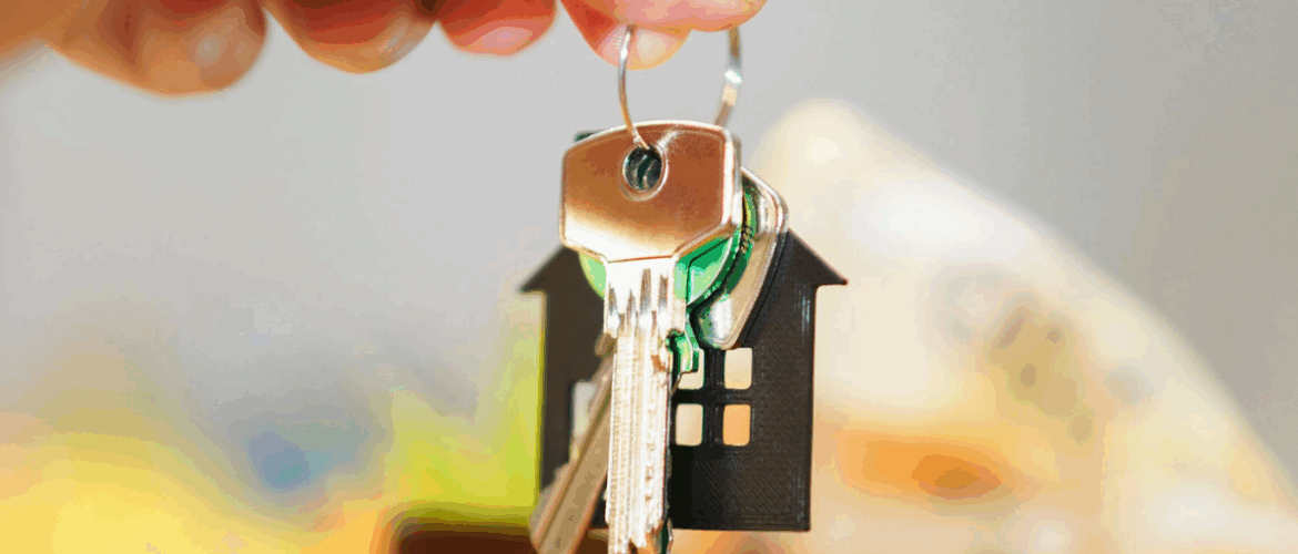 imagem de uma mão segurando um molho de chaves com notas de dinheiro desfocadas ao fundo