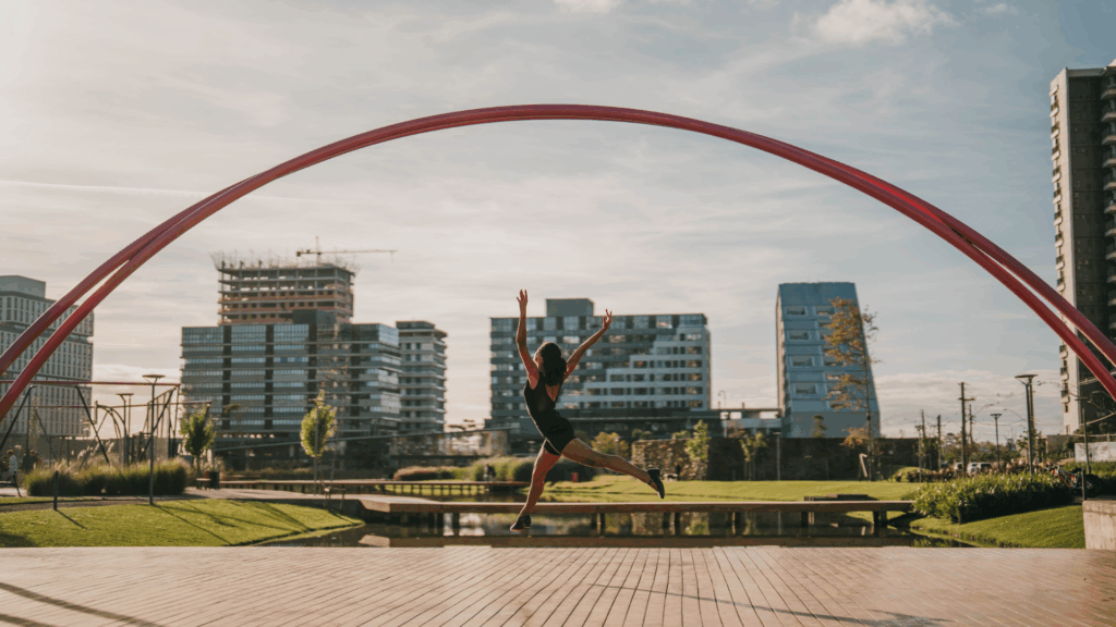 menina dançando, dando um salto no ar, com o parque ao fundo