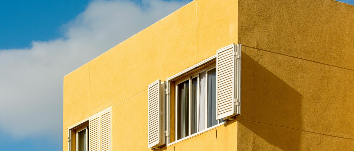 fachada de prédio amarela com janelas brancas e céu claro ao fundo