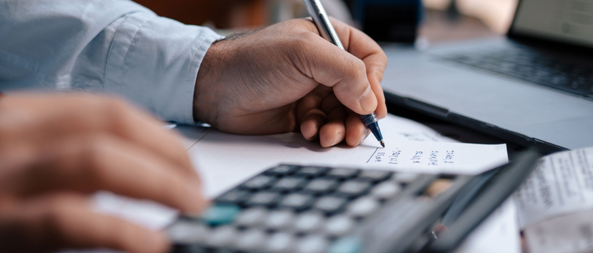 Mãos de um homem segurando uma caneta e fazendo contas em uma calculadora