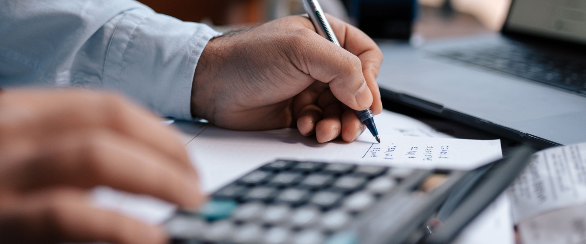 Mãos de um homem segurando uma caneta e fazendo contas em uma calculadora